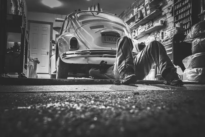 A mechanic lying on the floor of a garage working underneath a classic car