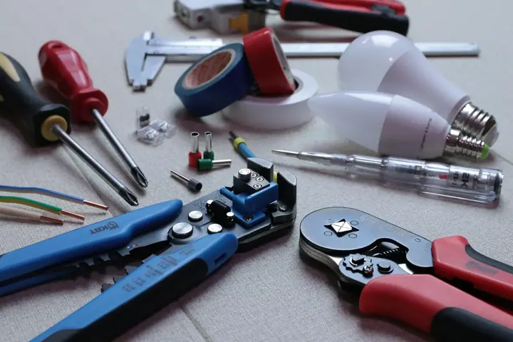Electrician's tools laid out: wire strippers, crimpers, screwdrivers, tape and light bulbs