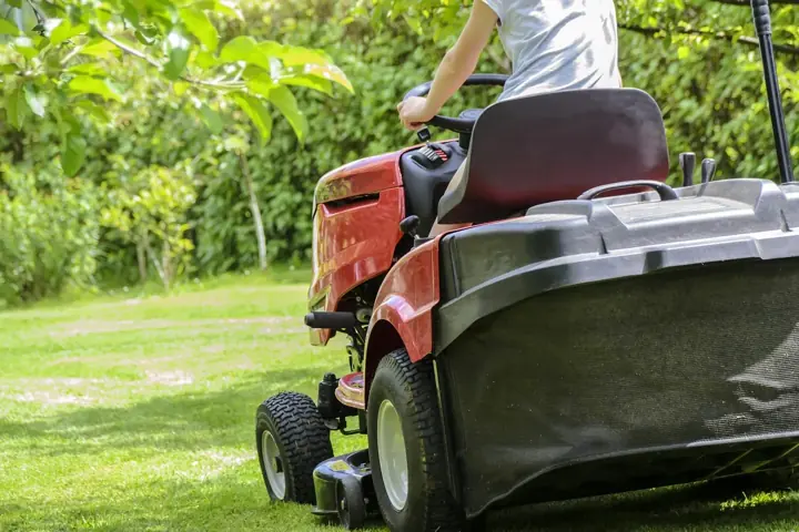 A red riding mower cutting a bright green lawn