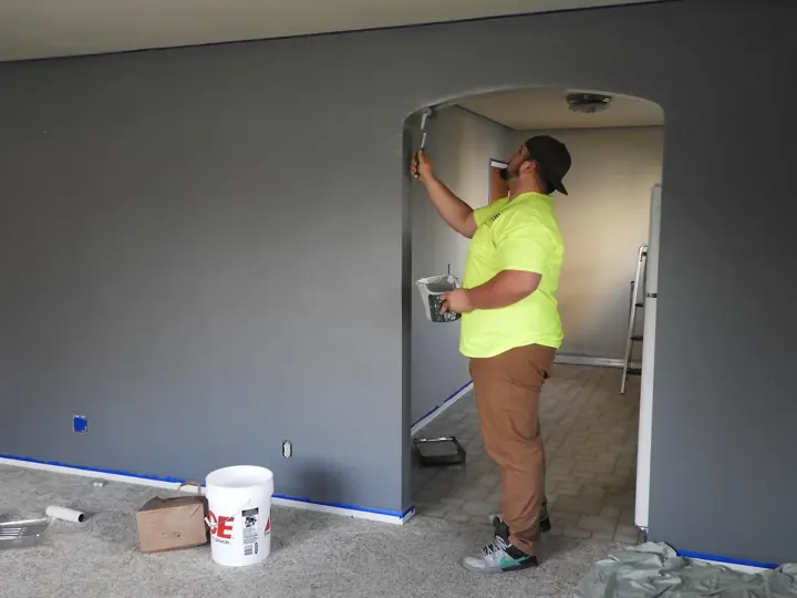 A painter working on a freshly painted gray interior wall around an archway