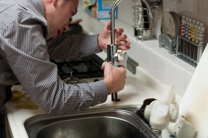 A plumber leaning over a kitchen sink installing a new faucet