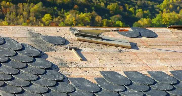 A roof being repaired, with new slate shingles laid out next to roofing tools