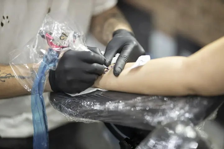 A tattoo artist in black gloves working on a client's forearm